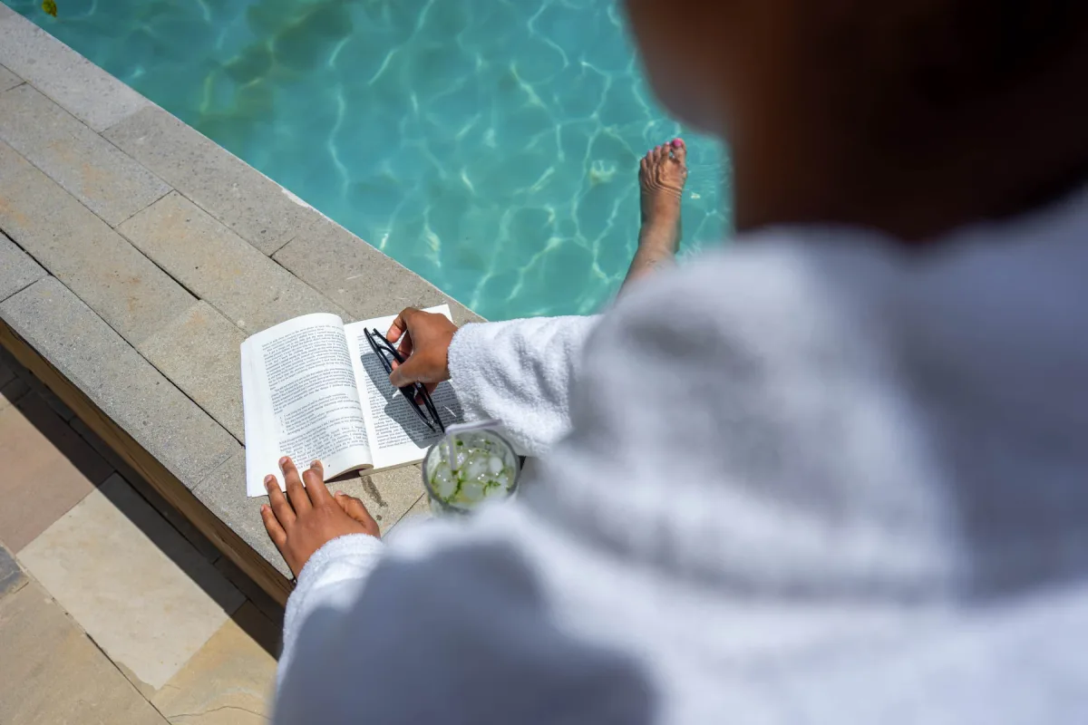 A guest reading a book beside a sunlit swimming pool
