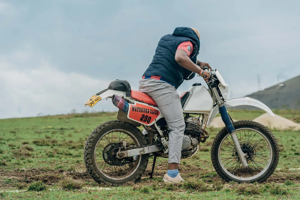 A motorcyclist standing with an off-road bike against an open green hillside